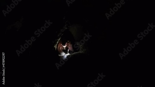 Female expedition caver crawls through tight dark cave passage photo
