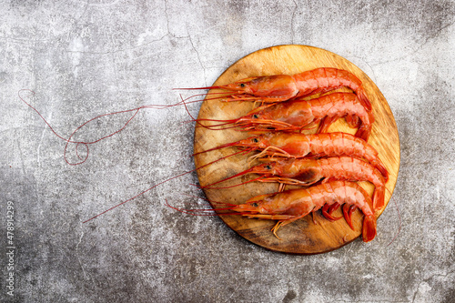 Argentinian raw red prawns (shrimps) with heads on a round wooden cutting board on a dark grey background. Top view, flat lay