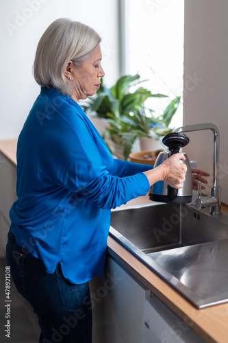 Mature woman pouring water into kettle photo