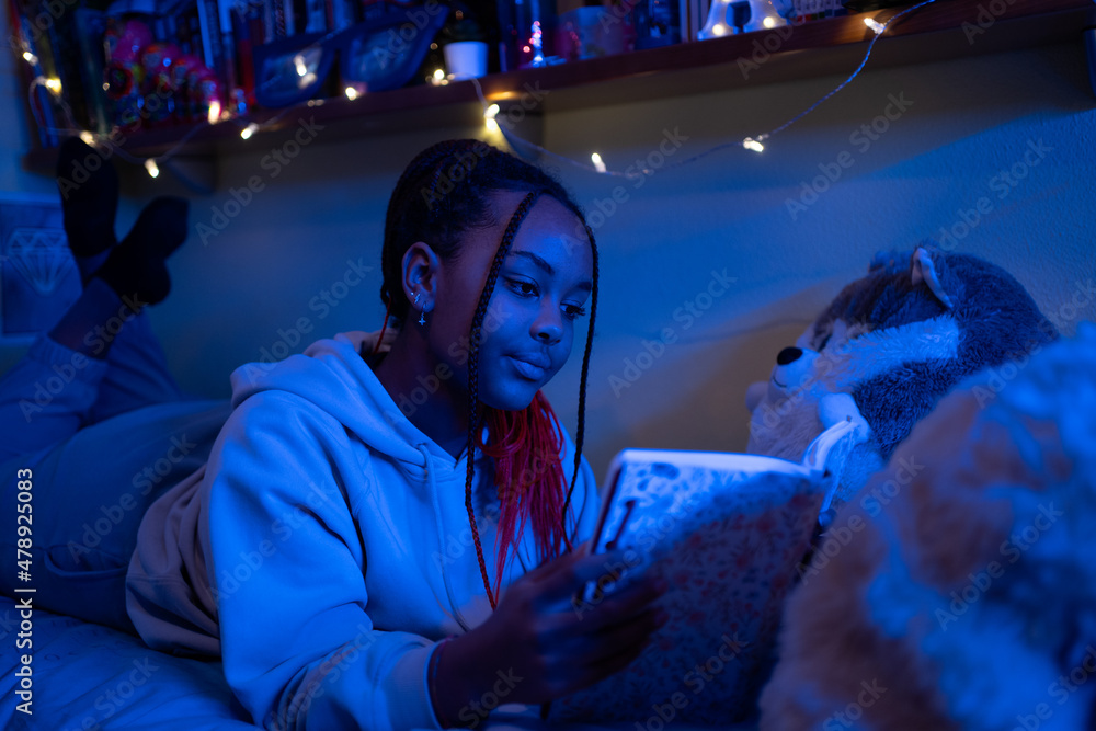 Teen Black Kid Reading A Book In Her Bedroom At Night. Teen Black Kid Reading A Book In Her Bedroom At Night.
