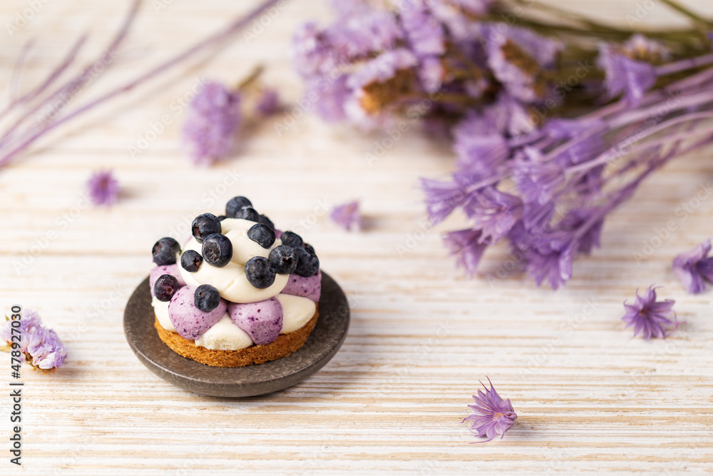 White chocolate and blueberry sable tartelette on a white drift wood table with purple dry flowers background.
