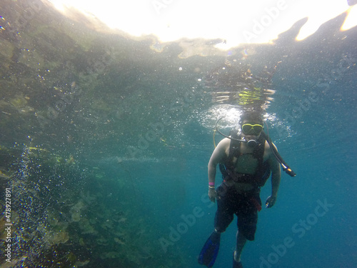 Latino adult man dives underwater with scuba equipment oxygen tank, visor, fins, enjoys sports and entertainment activity 