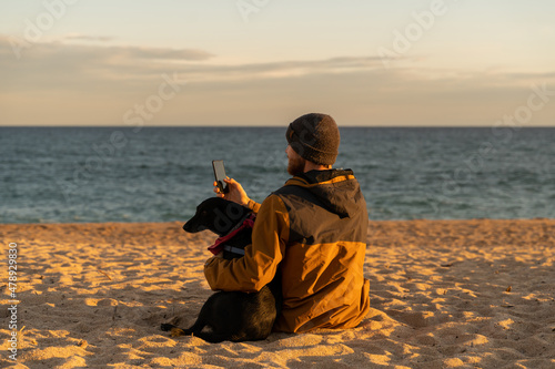 man and dog sitting at beach on sunset photo