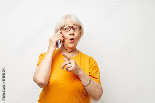 elderly woman in a yellow t-shirt posing communication by phone light background