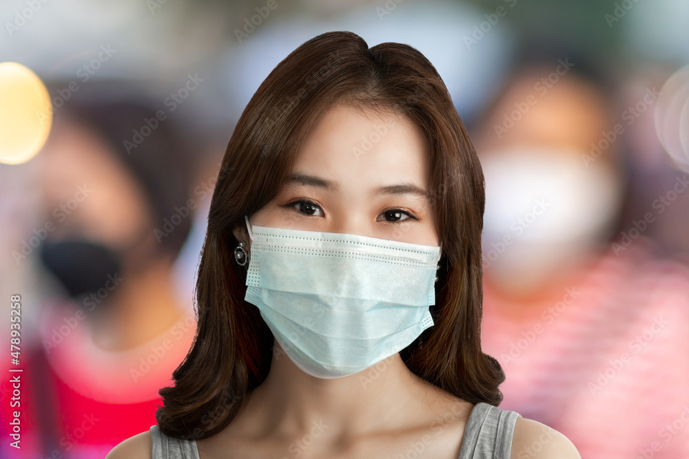 A close-up of a young Asian woman with smile under a sanitary face mask against coronavirus or COVID-19 at a street in an urban city. Virus and illness protection, sanitizer in a public crowded place