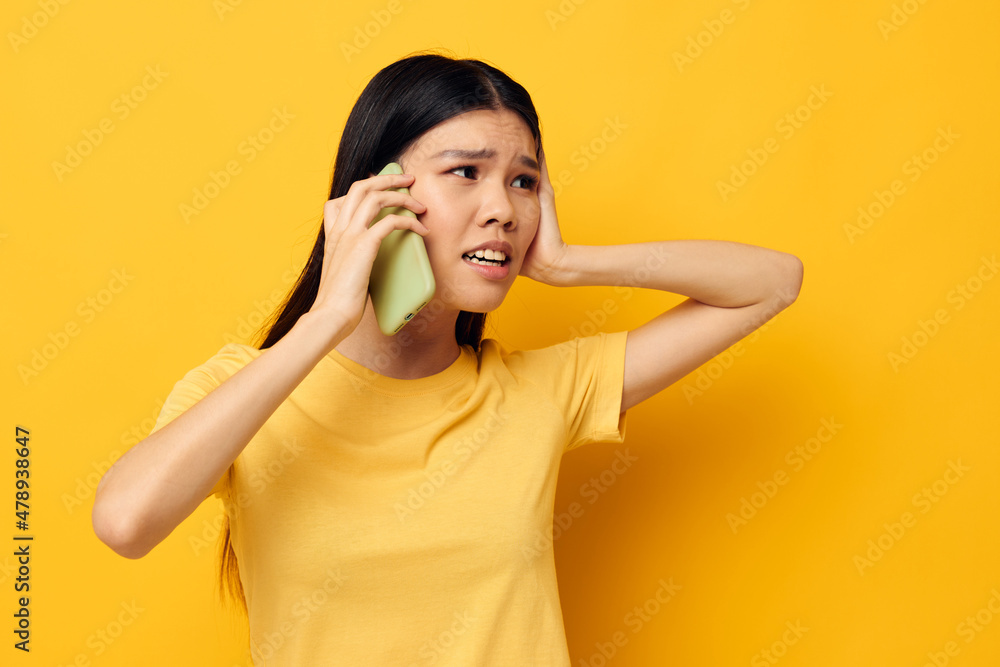 Charming young Asian woman communicates on the phone emotions yellow background unaltered Charming young Asian woman communicates on the phone emotions yellow background unaltered