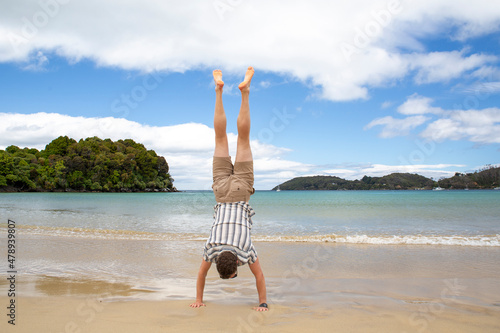 A traveler performs a handstand in the golden sand of Bathing Beach, Oban, Stewart Island, New Zealand. photo