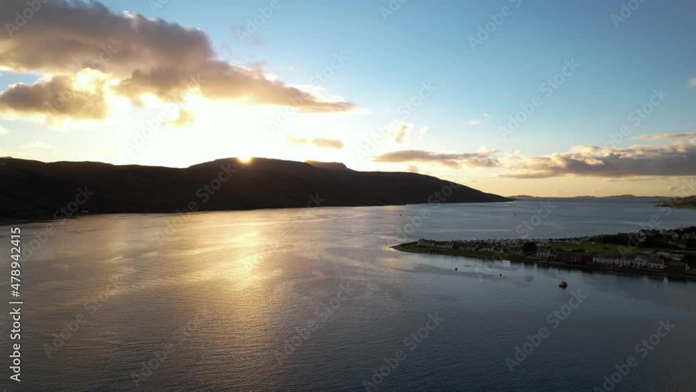 Beautiful sunset behind the black silhouette of the mountains in Ullapool on a partly cloudy day. Wide drone panning shot Beautiful sunset behind the black silhouette of the mountains in Ullapool on a partly cloudy day. Wide drone panning shot