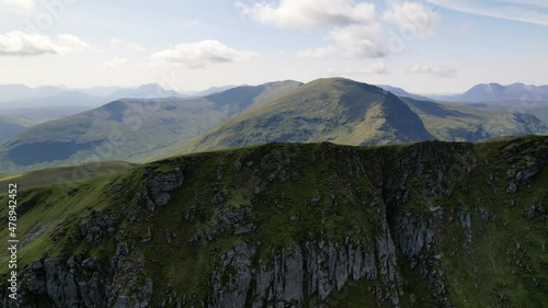 A Male standing on the top of green mountain ridge Fannichs between the peaks of the Scottish highlands on a sunny day. Slowly drone panning shot photo