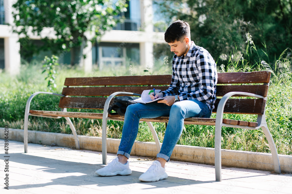 young boy studying while sitting on a bench in the sun