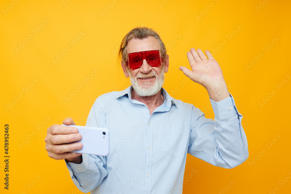 Naklejka premium Senior grey-haired man in fashionable red glasses with a phone isolated background
