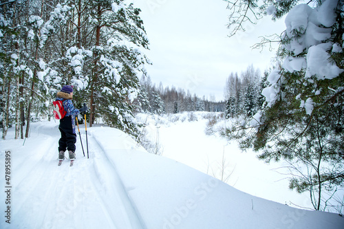 A child in a winter overalls on a ski trip in the winter forest. Beautiful winter landscape after snowfall