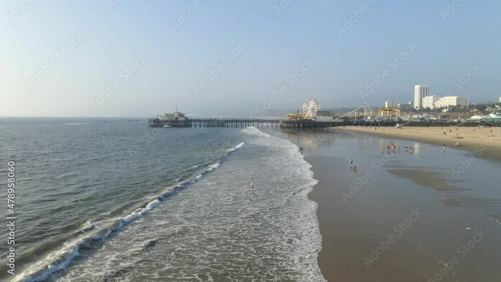 aerial view of people walking at the beach and swimming in the ocean waves rolling at Santa Monica Pier
