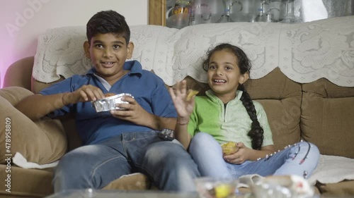 Kids laughing by watching tv or television while eating at home - concept of weekend or holiday entertinment, leisure activities and togetherness photo