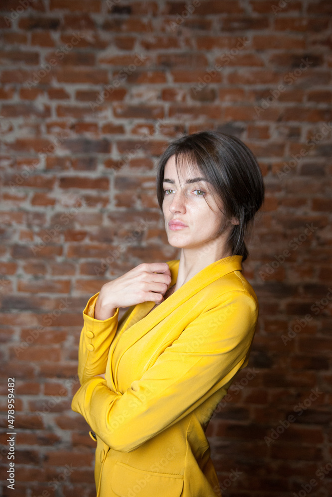 Beautiful russian girl in   bright yellow jacket against   brick wall