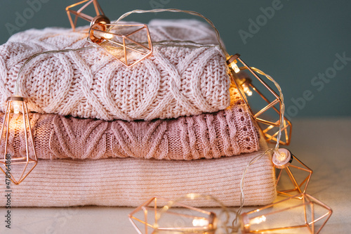 Stack of knitted sweaters with fairy lights garland. photo