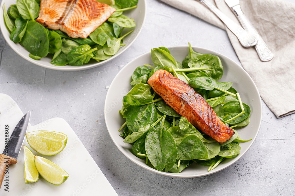 Grey bowl with fresh green raw spinach and fried red salmon, lime slices on grey concrete surface Grey bowl with fresh green raw spinach and fried red salmon, lime slices on grey concrete surface