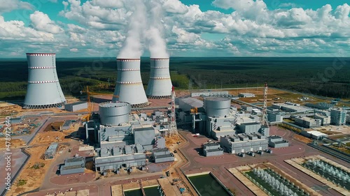 The flight of a drone over power units and cooling towers with steam and smoke from a nuclear power plant on a clear sunny day.