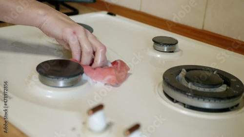 A Female Hand is Washing, Cleaning Dirty Hot the Hob with a Sponge and Foam. A housewife or housekeeper wipes off burnt dirt, residual fat after cooking, using a detergent. Smoke on the burners. 4K. photo