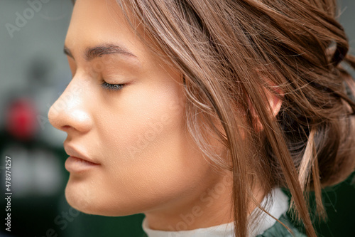 Portrait of a sensual young caucasian woman with closed eyes showing makeup tan on her face and hairstyle in a beauty salon