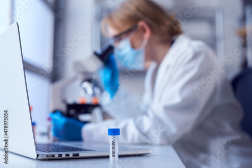 Female Lab Worker Wearing Lab Coat Working On Vaccine In Laboratory With Laptop And Microscope