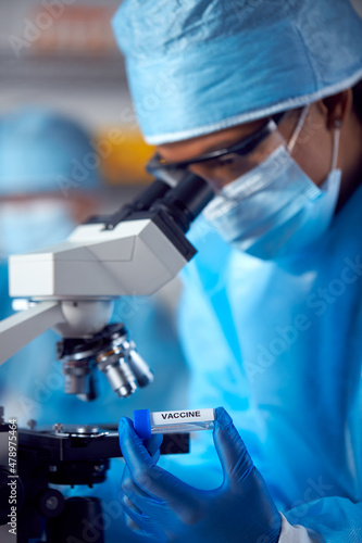 Close Up Of Female Lab Worker Wearing PPE Researching Vaccine With Microscope