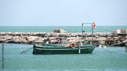 Fishing boats near the pier, and man walking on the pier with strong wind in Minturno, Lazio, Italy.