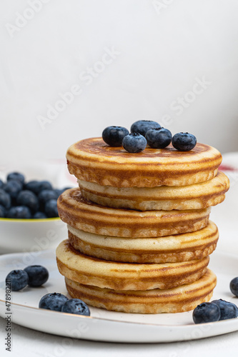 Stack of delicious pancakes on white plate with fresh blueberries on and in bowl. Side view, Copy space