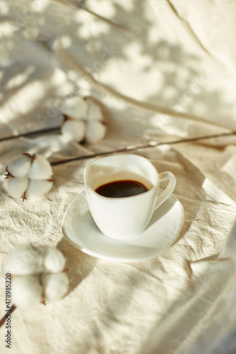 Cup of coffee in bed with cotton flowers, morning mood, Organic and natural linen cotton textile bedclothes, copy space.