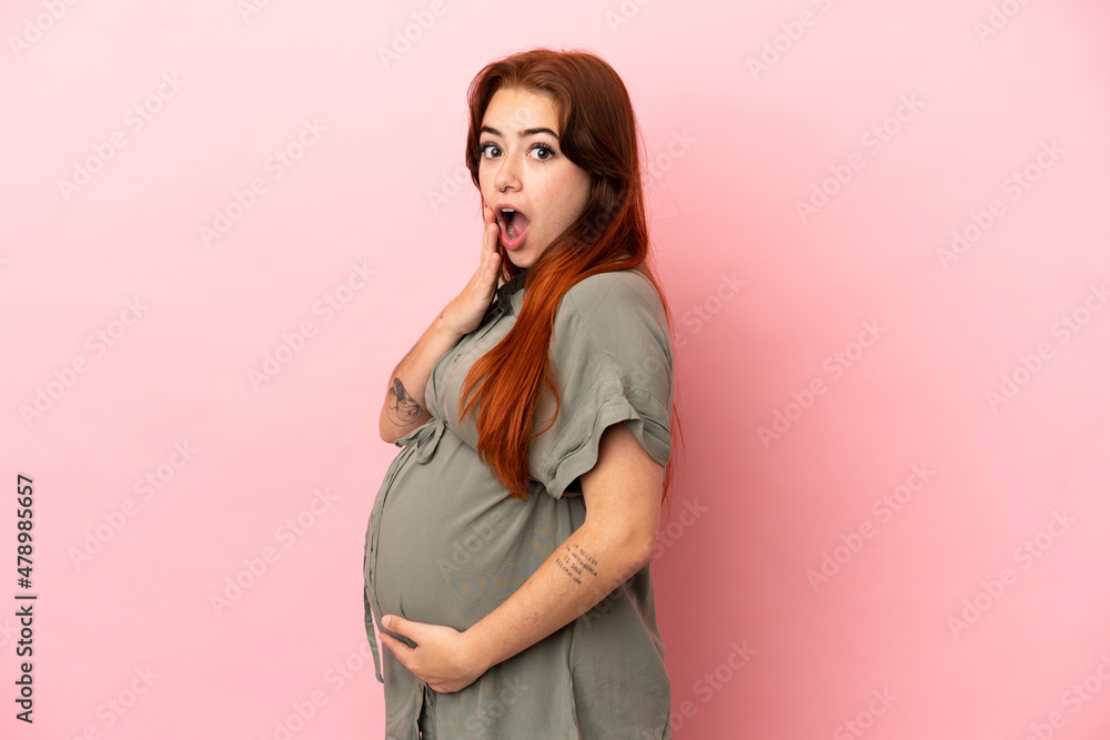 Young redhead caucasian woman isolated on pink background pregnant and doing surprise gesture Young redhead caucasian woman isolated on pink background pregnant and doing surprise gesture