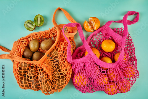 Flat lay Mesh grocery shopping eco friendly bag with kiwi and tangerine fruits on green canvas background, Zero waste cconcept, Local farmers market, top view, copy space, Plastic free items.