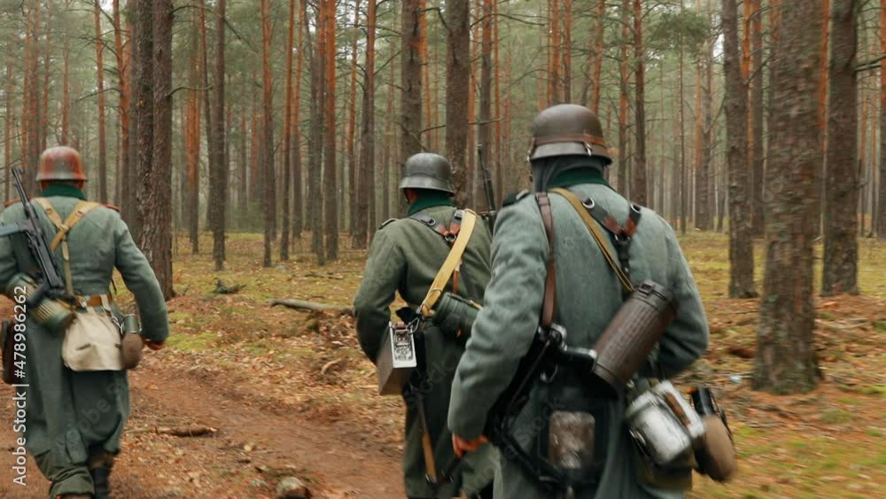 Re-enactors German Wehrmacht Infantry Soldier In World War II Marching Walking Along Forest Road In Autumn Day. Group of Soldiers Marching In Forest Re-enactors German Wehrmacht Infantry Soldier In World War II Marching Walking Along Forest Road In Autumn Day. Group of Soldiers Marching In Forest