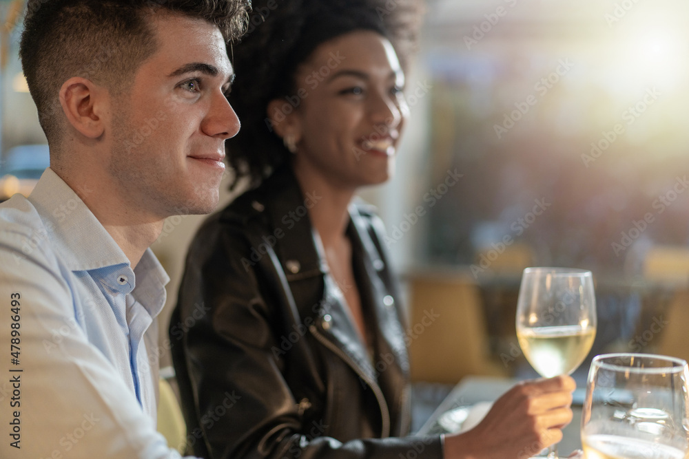 Multiracial couple sitting at restaurant drinking white wine