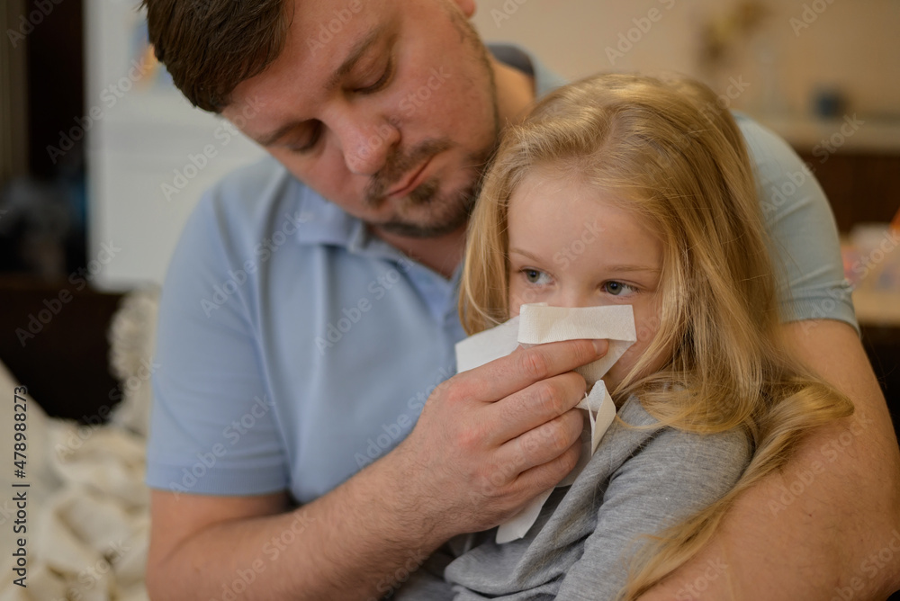 dad wipes his sick child's nose with a white disposable paper napkin at home. The father suspects that his daughter is ill. The child is not feeling well. the concept of equality in the family between
