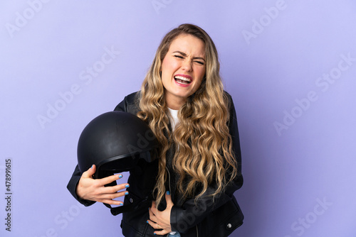 Young Brazilian woman holding a motorcycle helmet isolated on purple background smiling a lot