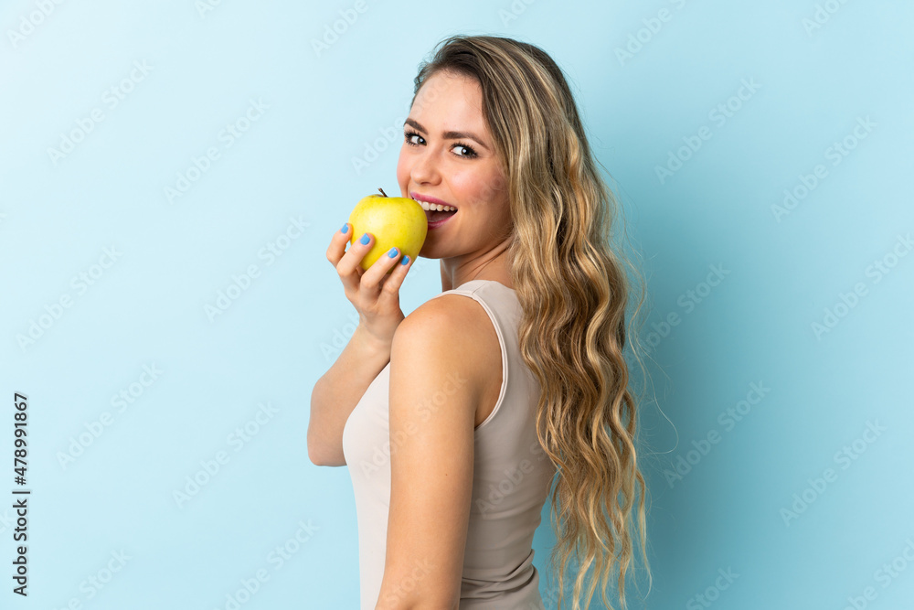 Young Brazilian woman isolated on blue background eating an apple Young Brazilian woman isolated on blue background eating an apple