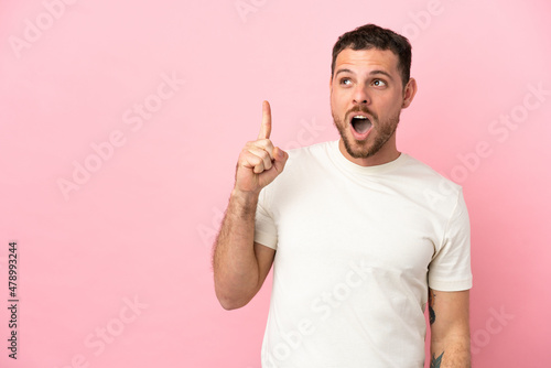 Young Brazilian man isolated on pink background thinking an idea pointing the finger up