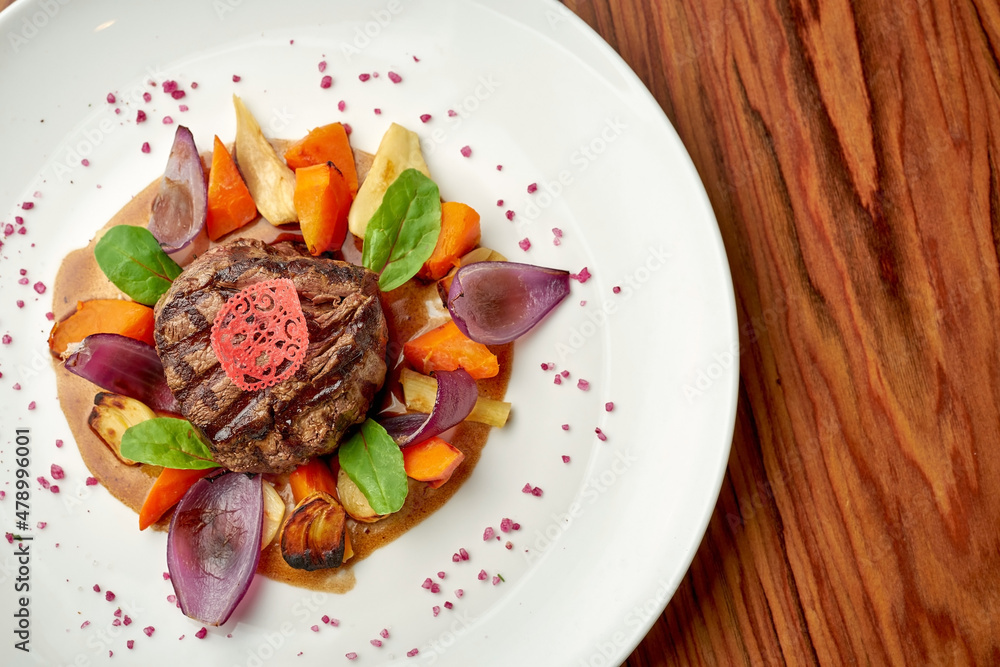 Beef fillet mignon with baked onions and vegetables in a white plate on a wooden background Beef fillet mignon with baked onions and vegetables in a white plate on a wooden background