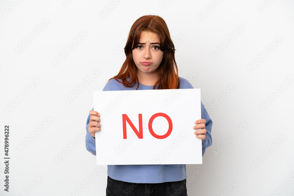 Young redhead woman isolated on white background holding a placard with text NO with sad expression Young redhead woman isolated on white background holding a placard with text NO with sad expression