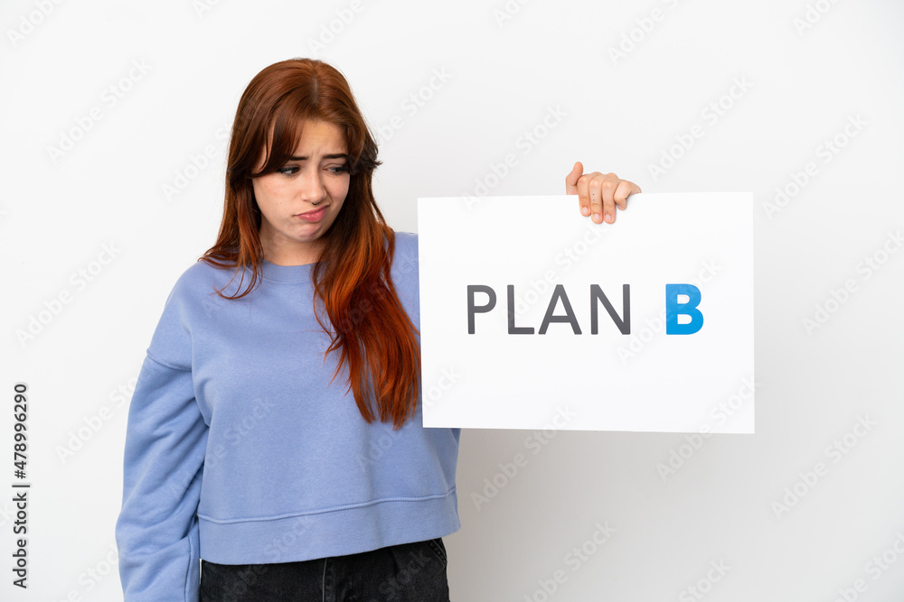 Young redhead woman isolated on white background holding a placard with the message PLAN B with sad expression Young redhead woman isolated on white background holding a placard with the message PLAN B with sad expression