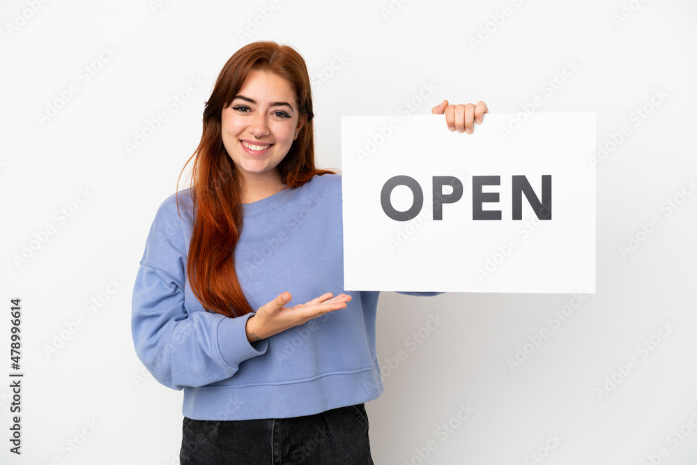 Young redhead woman isolated on white background holding a placard with text OPEN and pointing it Young redhead woman isolated on white background holding a placard with text OPEN and pointing it