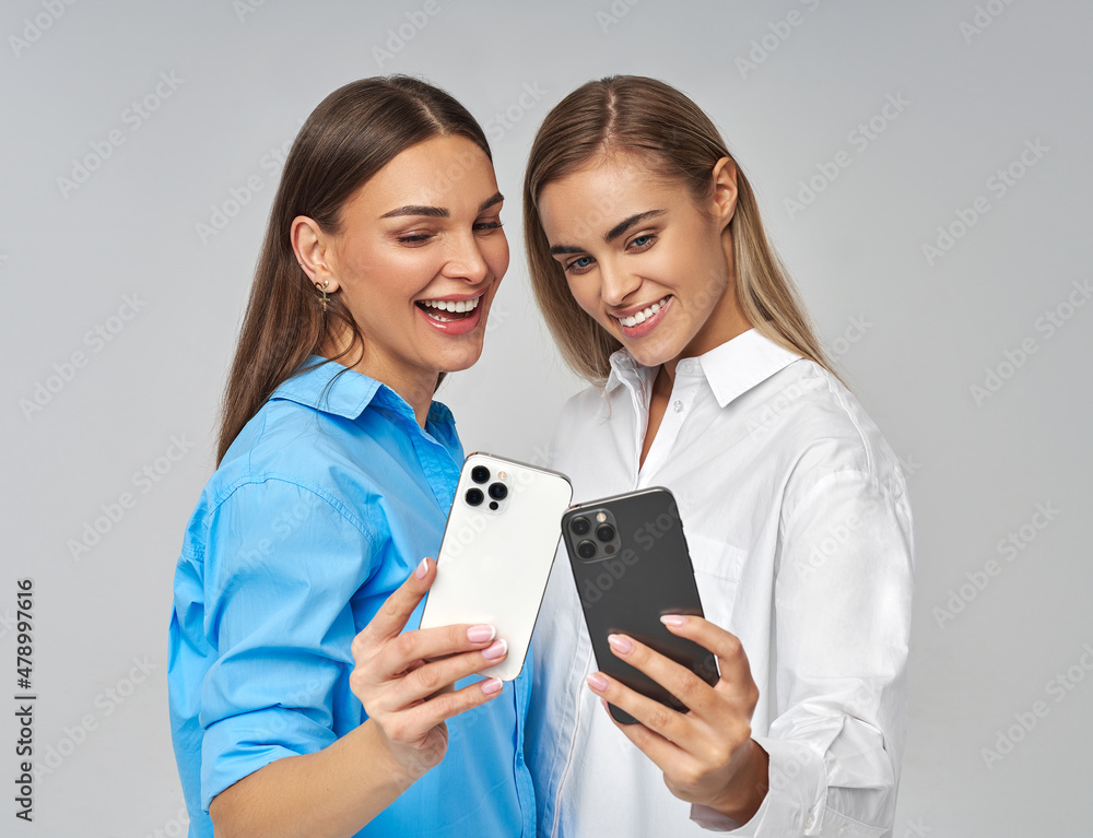 Two beautiful cheerful womem taking a selfie, isolated on gray background Two beautiful cheerful womem taking a selfie, isolated on gray background