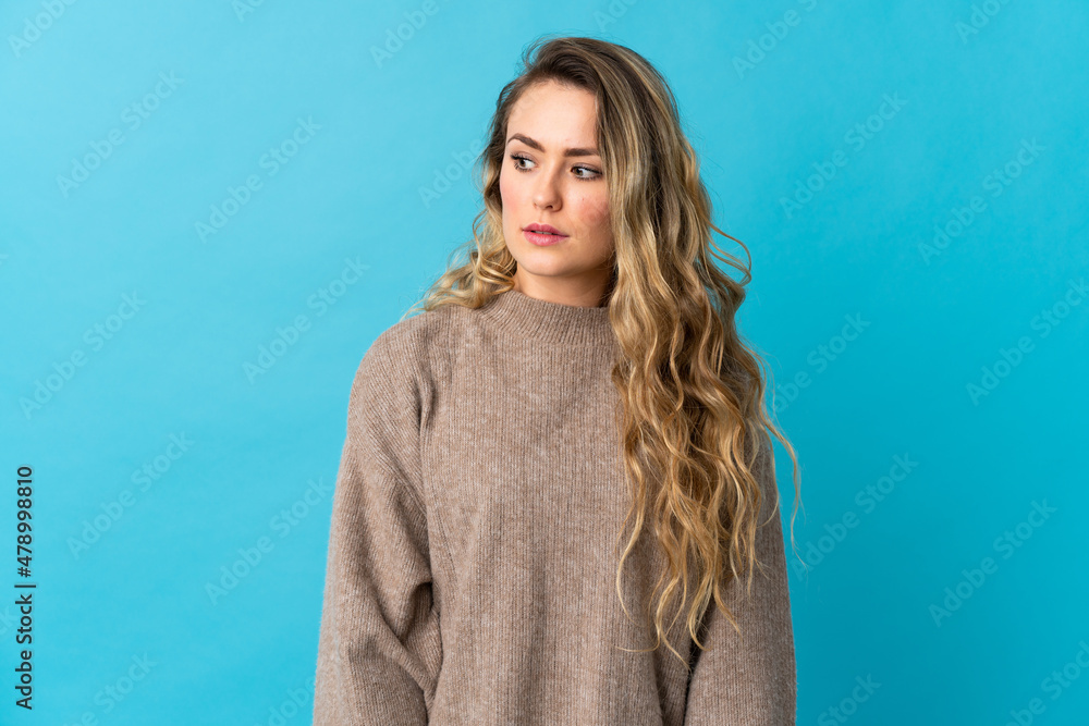 Young Brazilian woman isolated on blue background making doubts gesture looking side Young Brazilian woman isolated on blue background making doubts gesture looking side