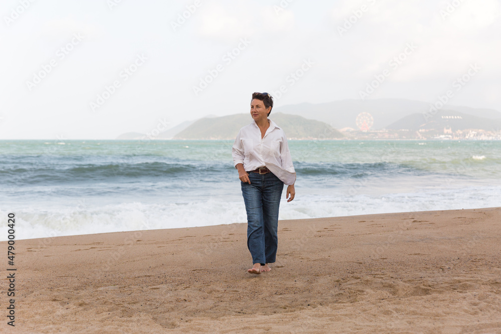 Portrait of a mature woman walking on the beach looking at the sea. Relaxed old lady strolling on the beach