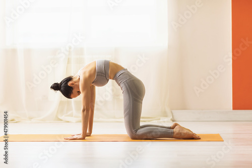Woman practicing yoga, doing the exercise marjariasana, cat pose, exercising on the rug in the studio against the wall photo