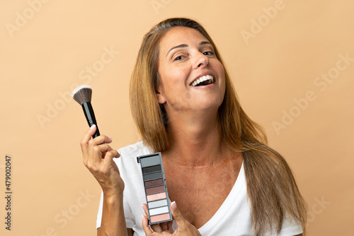 Middle age brazilian woman isolated on beige background with makeup palette and happy