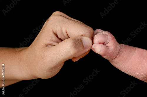 Small closed hand of newborn baby bumping his fist with his mother's hand.
