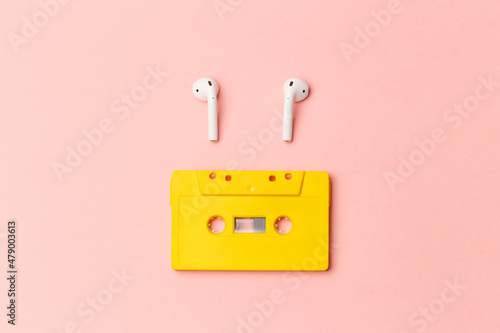 Yellow audio cassette and modern wireless headphones on a pink background. Comparison of old and new technologies. Listening to music, music lovers. Top view. Flat lay