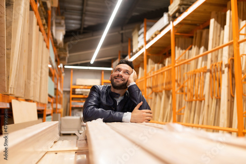 Obraz na plátně happy customer in a hardware store looks at racks with planks and wooden blocks,