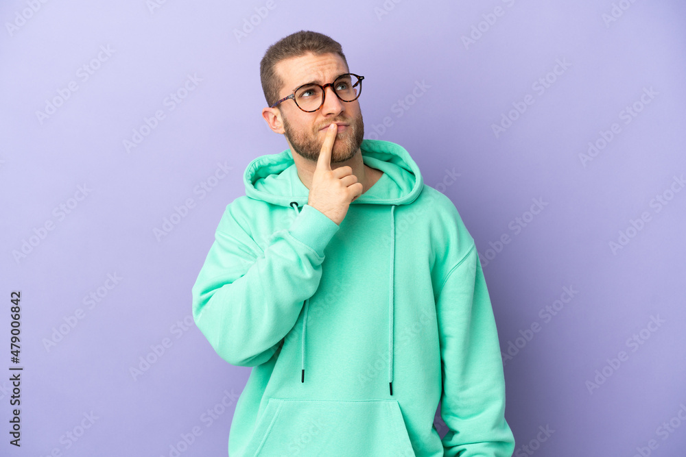 Young handsome caucasian man isolated on purple background having doubts while looking up